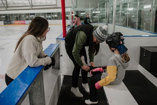 Adult tying laces on a child?s skate while another adult observes.