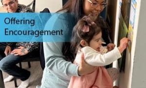 Parent lifts child up to place sticker on poster